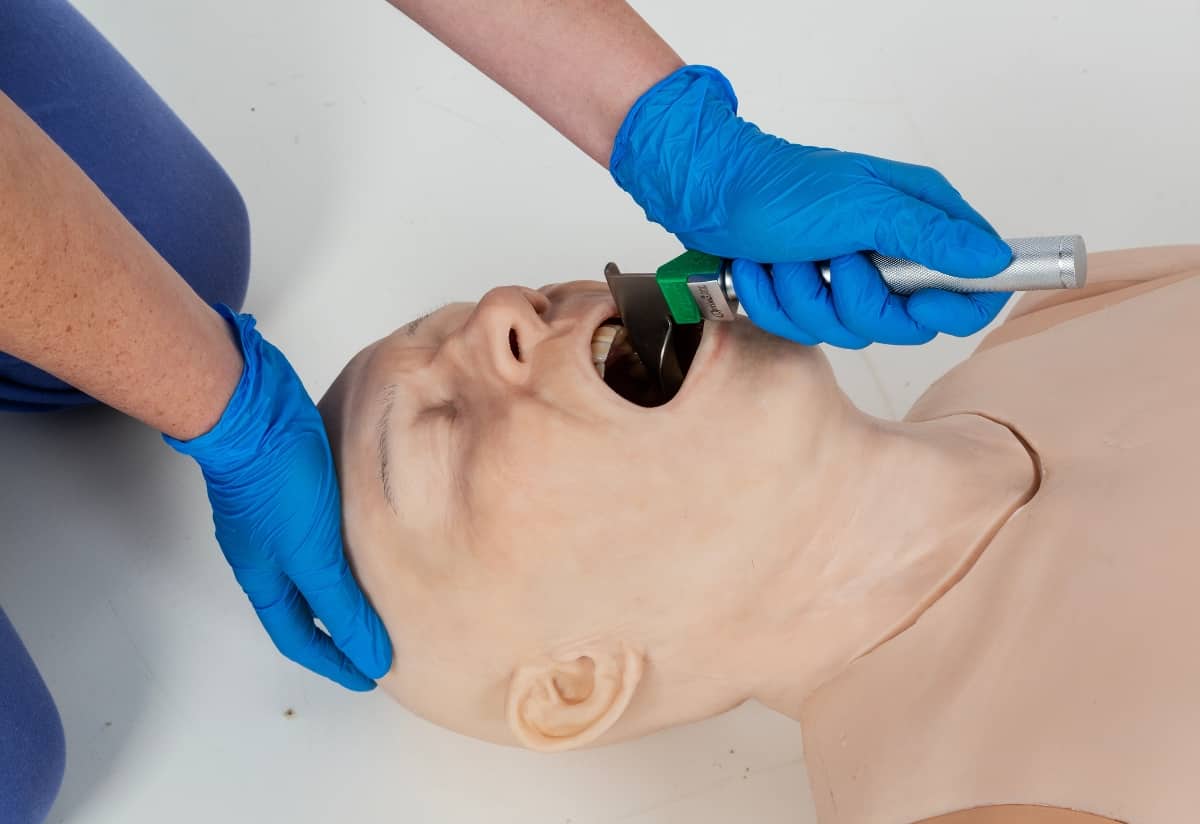 Instructor practising airway management on an ALS training manikin with a laryngoscope, demonstrating advanced CPR training techniques for paramedic training during cardiac arrest simulations.