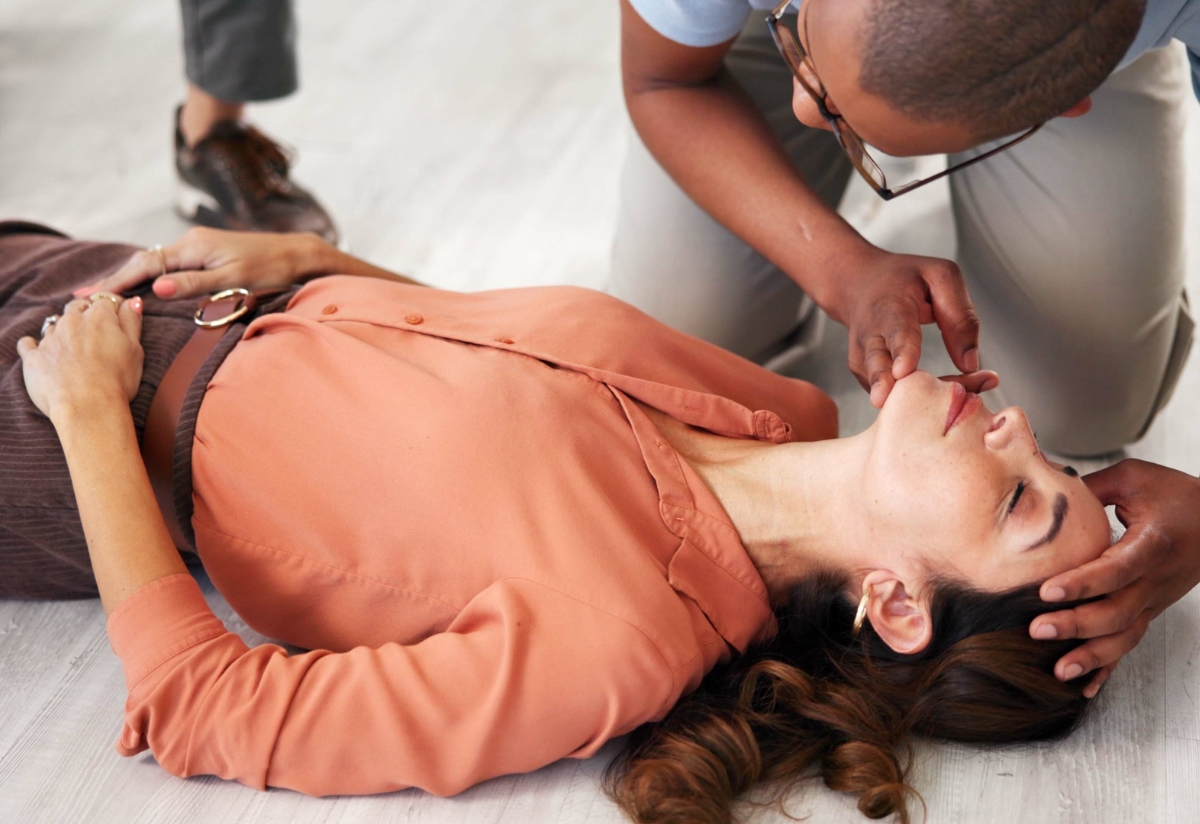 (EU) CPR Competence: First aider checking airway of an unconscious woman lying on the floor